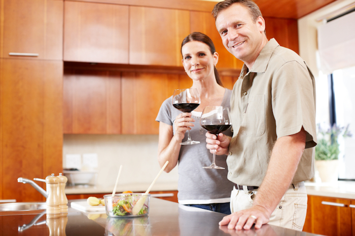 Happy mature couple smiling while standing in their kitchen and enjoying a glass of wine - portrait